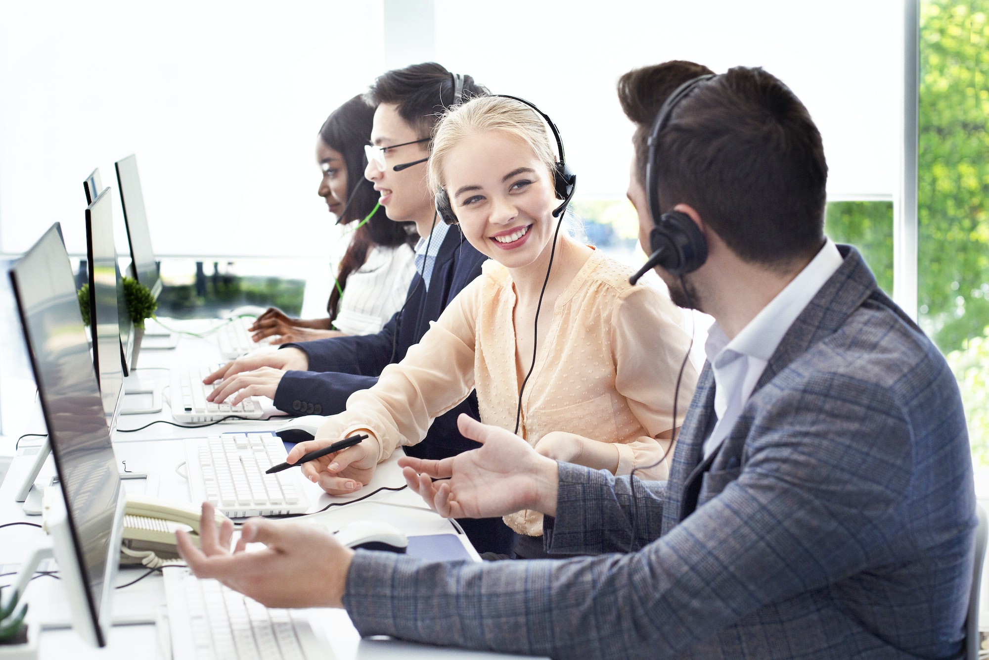 Smiling customer support workers communicating to solve client's problem together at call centre